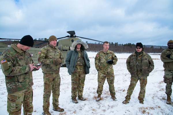 A man wearing a camouflage military uniform prepares for a parachute jump outside in a snow covered field.