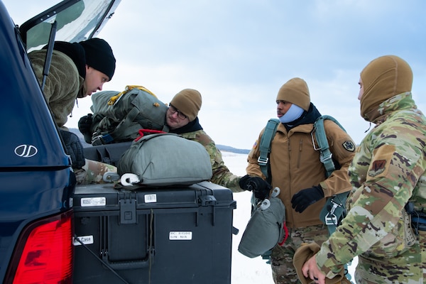 A man wearing a camouflage military uniform prepares for a parachute jump outside in a snow covered field.