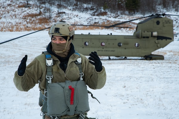 A man wearing a camouflage military uniform prepares for a parachute jump outside in a snow covered field.