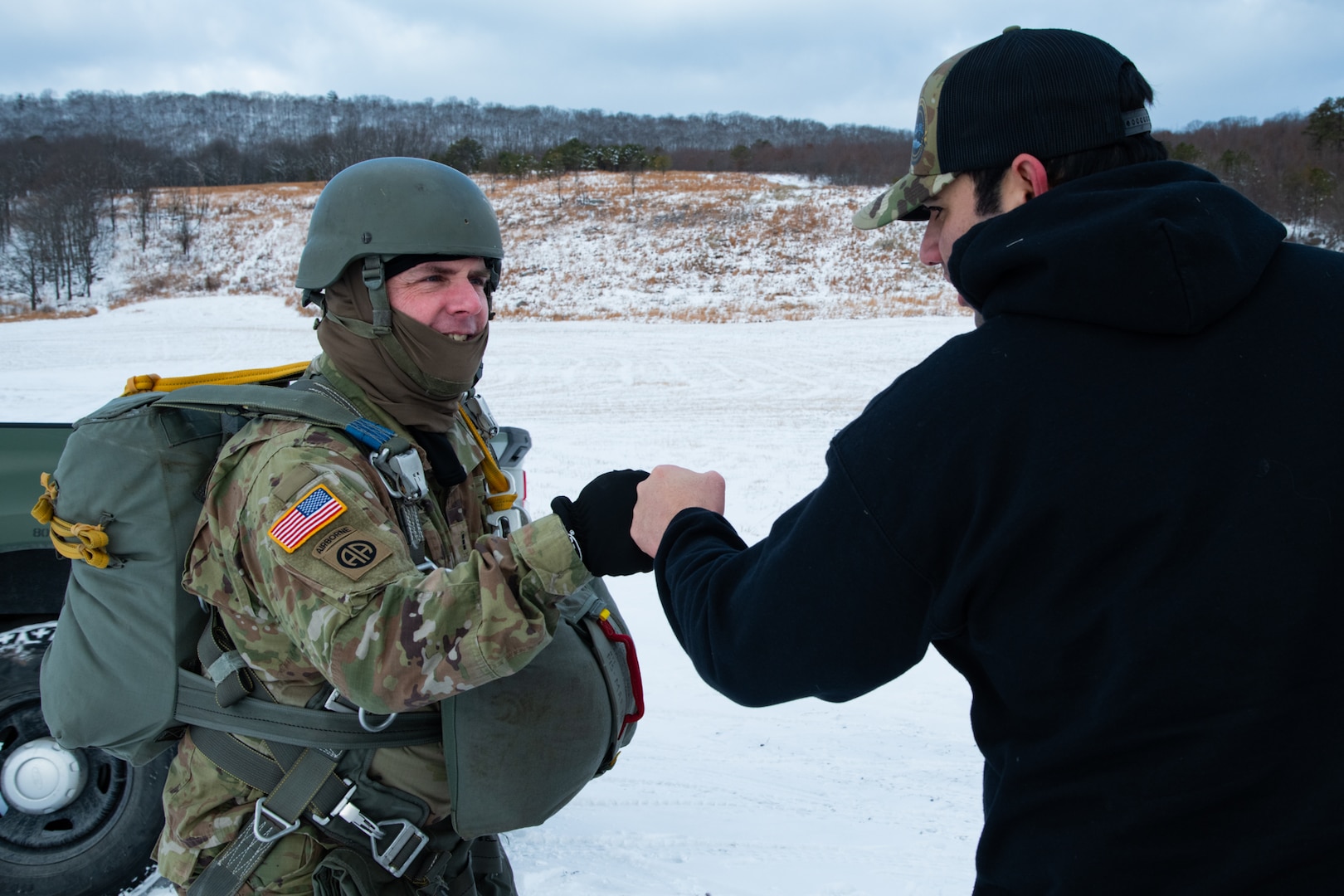 A man wearing a camouflage military uniform prepares for a parachute jump outside in a snow covered field.