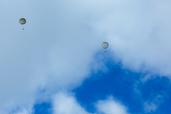 A man wearing a camouflage military uniform prepares for a parachute jump outside in a snow covered field.