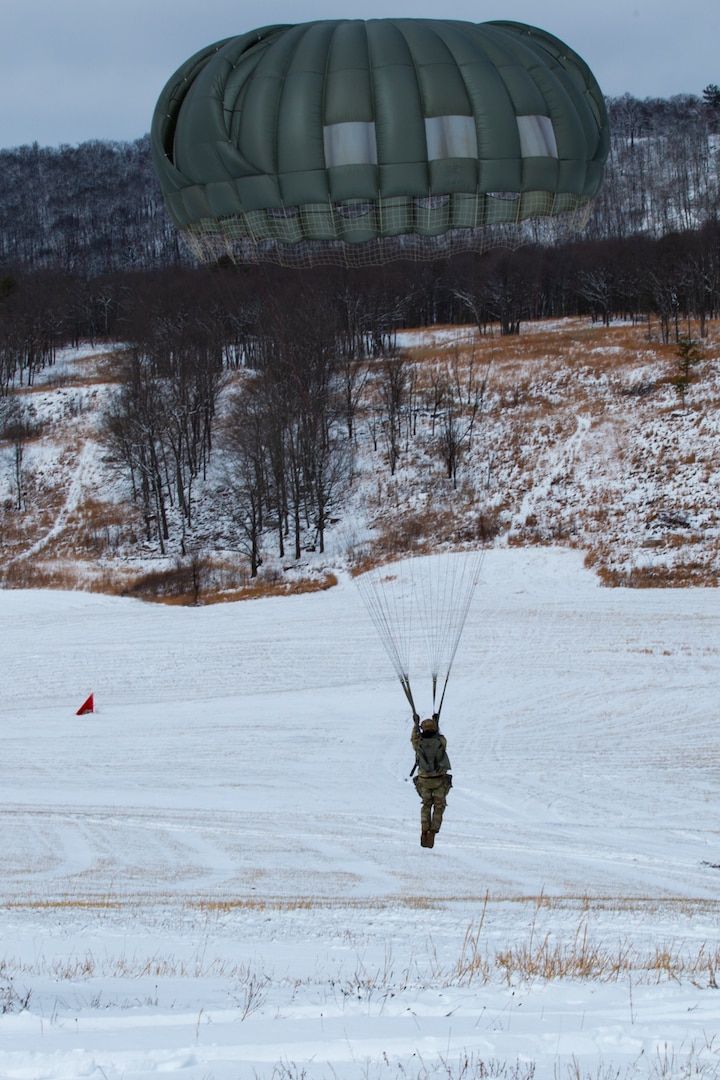 A man wearing a camouflage military uniform prepares for a parachute jump outside in a snow covered field.