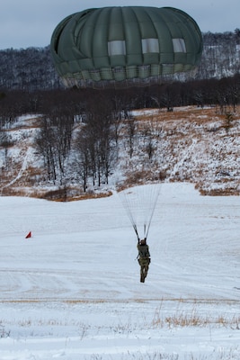 A man wearing a camouflage military uniform prepares for a parachute jump outside in a snow covered field.