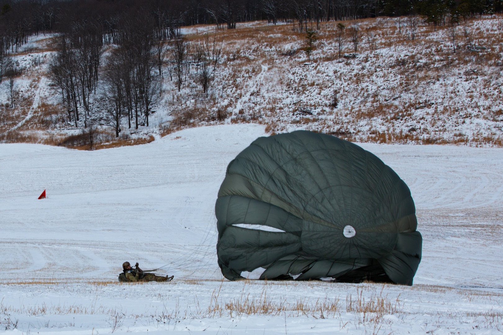 A man wearing a camouflage military uniform prepares for a parachute jump outside in a snow covered field.