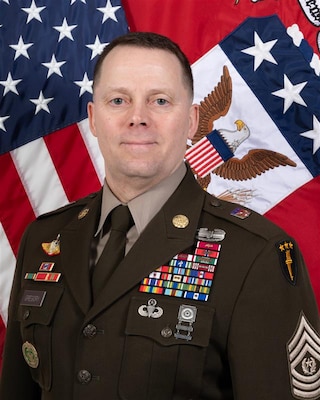Photo of a man in front of two military flags.