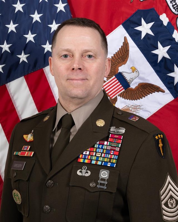 Photo of a man in front of two military flags.
