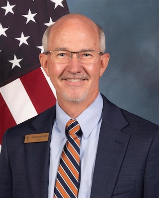 Photo of a man in front of a flag and blue background.