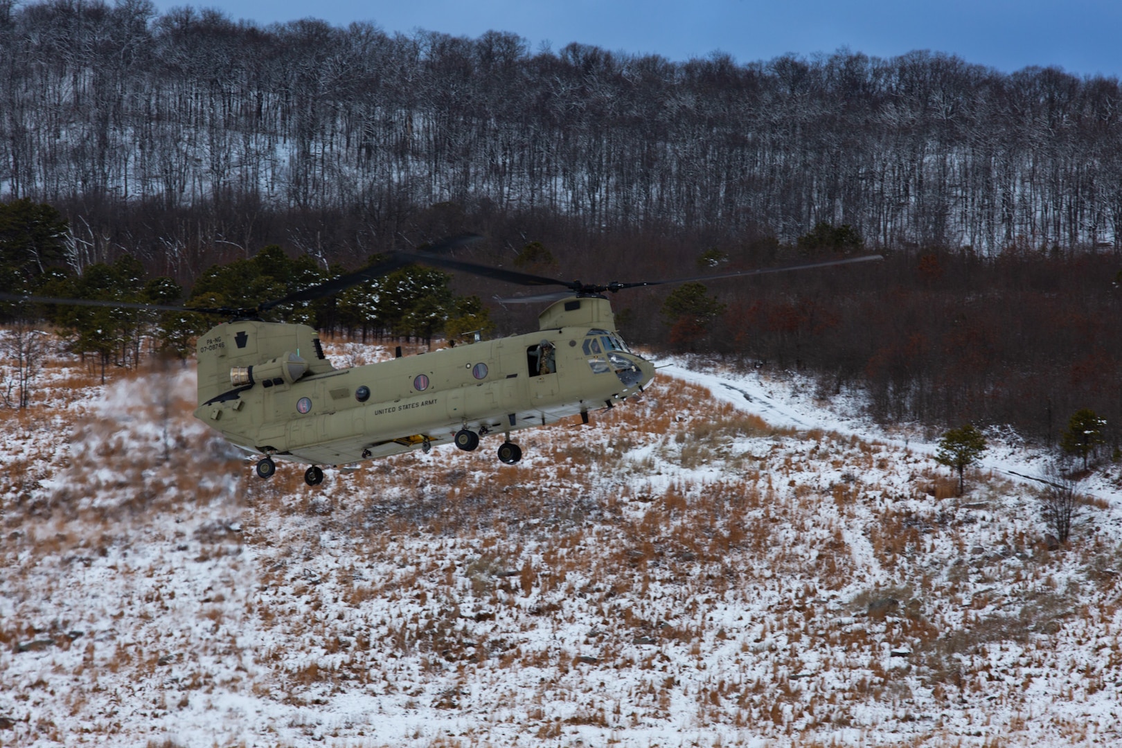 A man wearing a camouflage military uniform prepares for a parachute jump outside in a snow covered field.