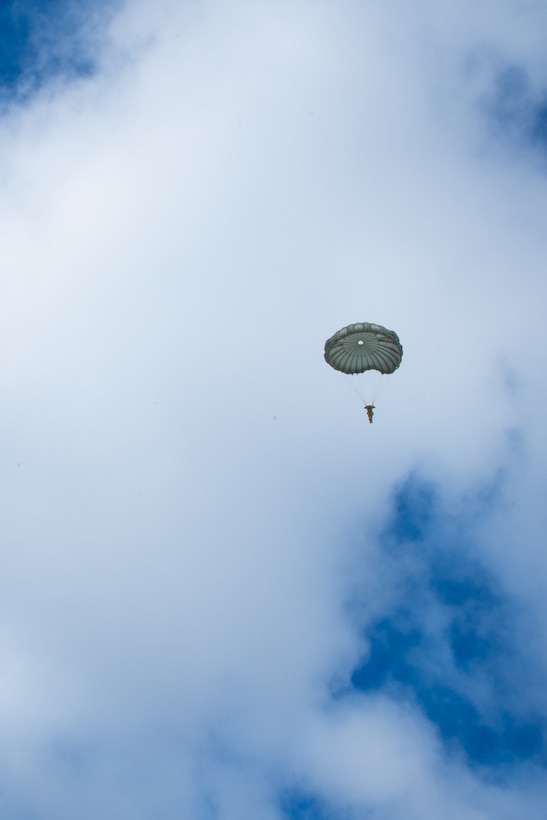 A man wearing a camouflage military uniform prepares for a parachute jump outside in a snow covered field.