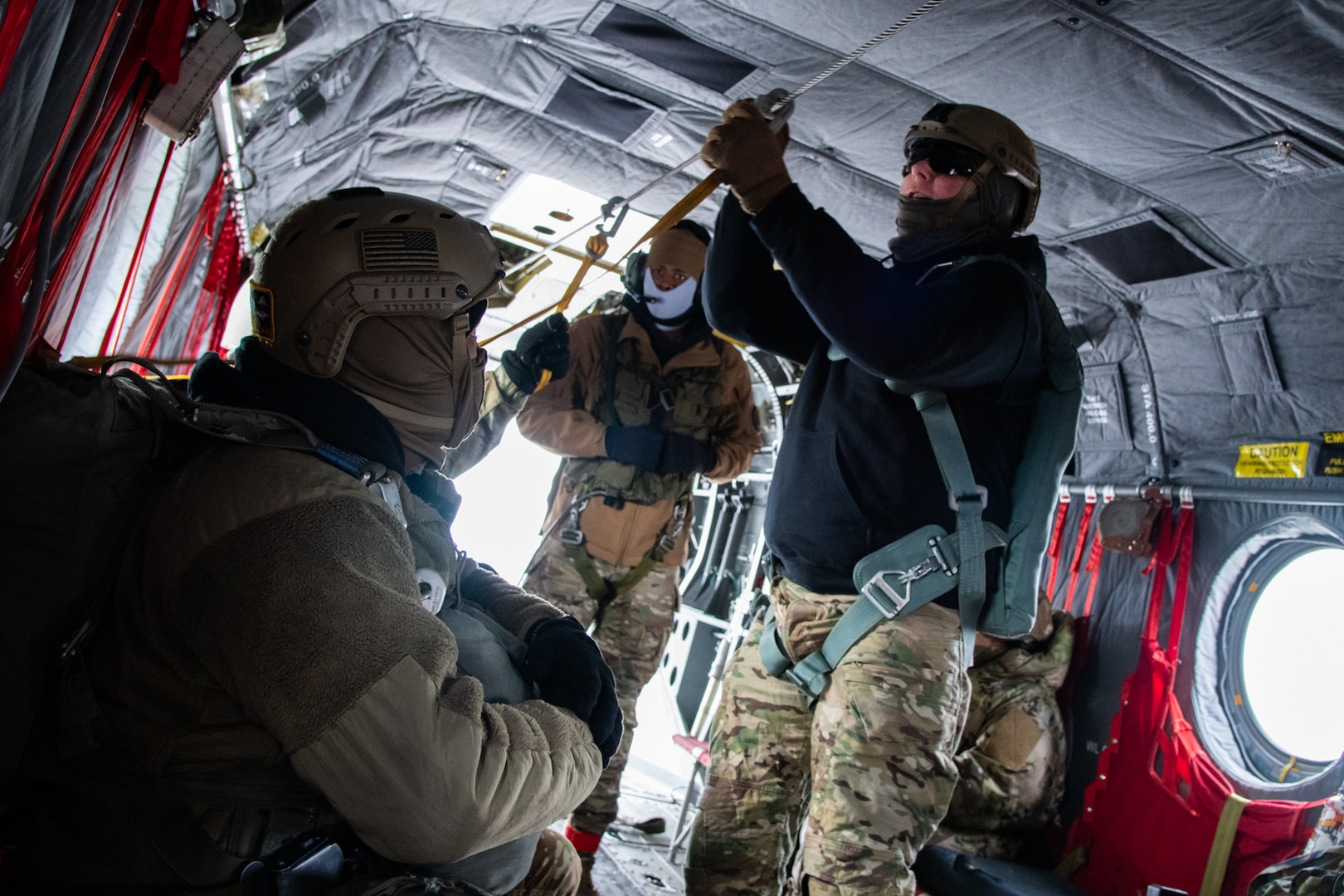 A man wearing a camouflage military uniform prepares for a parachute jump outside in a snow covered field.