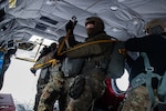 A man wearing a camouflage military uniform prepares for a parachute jump outside in a snow covered field.