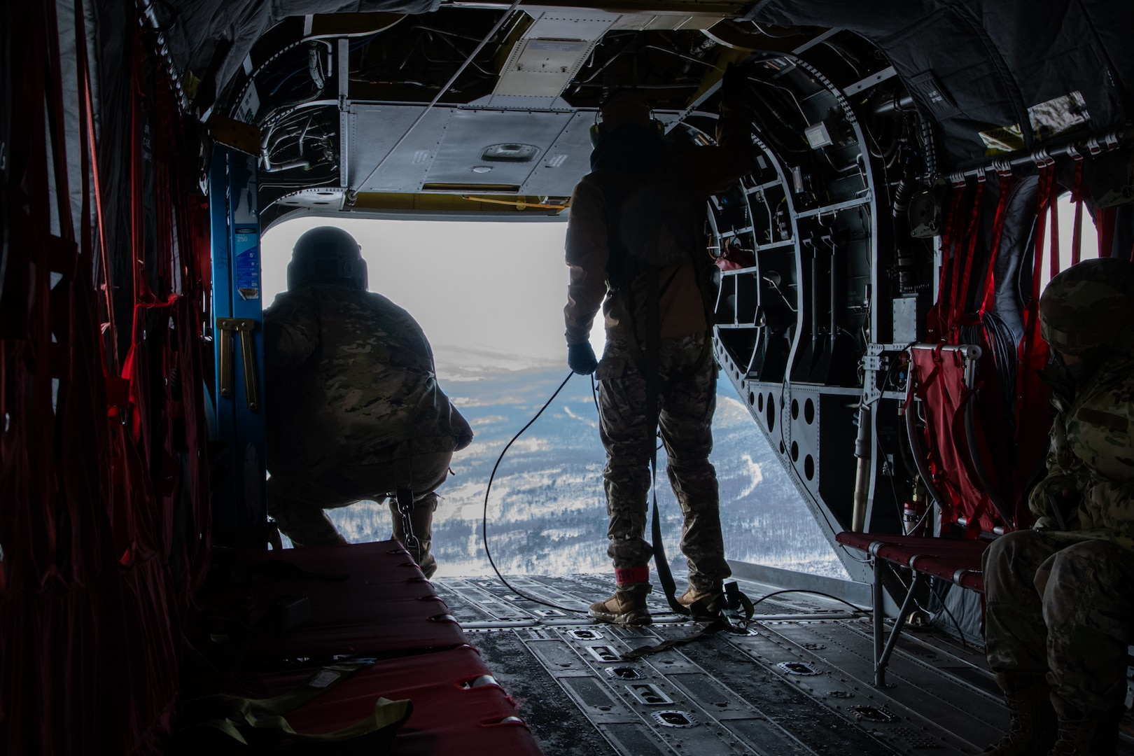A man wearing a camouflage military uniform prepares for a parachute jump outside in a snow covered field.