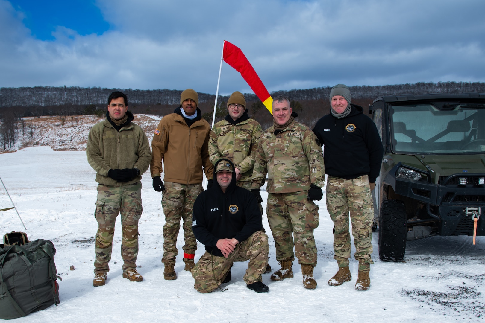 A man wearing a camouflage military uniform prepares for a parachute jump outside in a snow covered field.