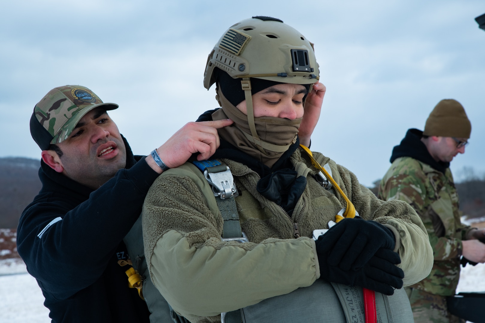 A man wearing a camouflage military uniform prepares for a parachute jump outside in a snow covered field.
