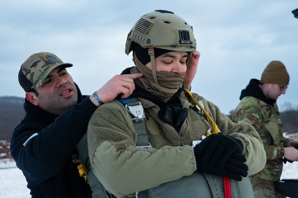 A man wearing a camouflage military uniform prepares for a parachute jump outside in a snow covered field.