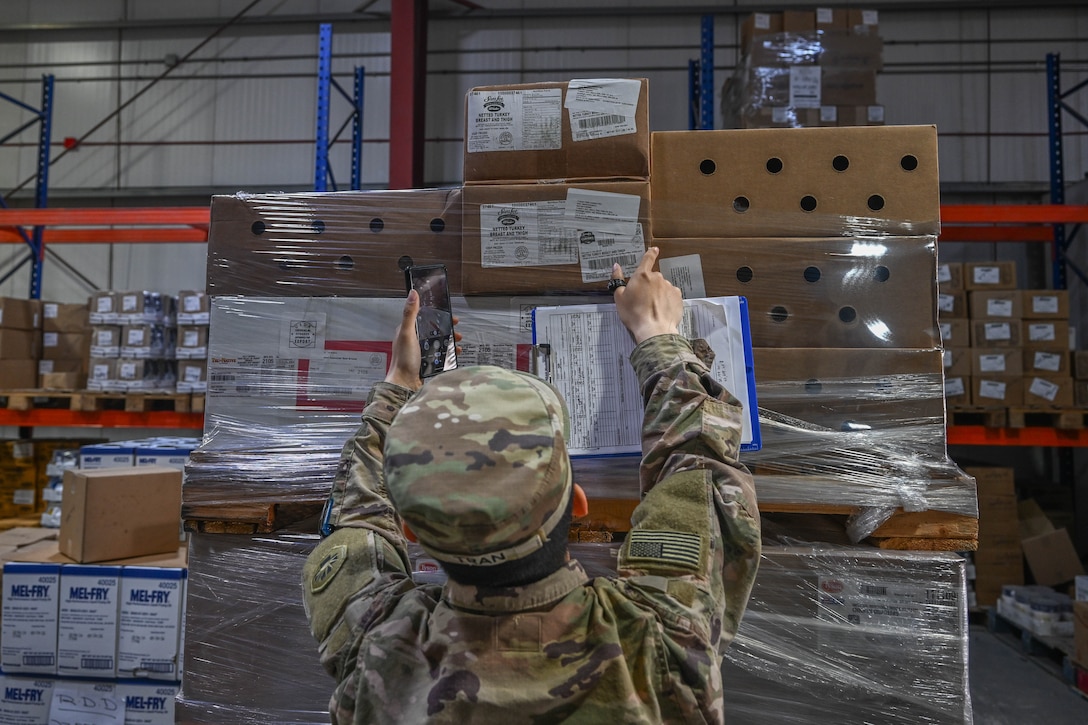 person in uniform reaches for boxes on pallet