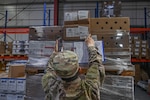 person in uniform reaches for boxes on pallet