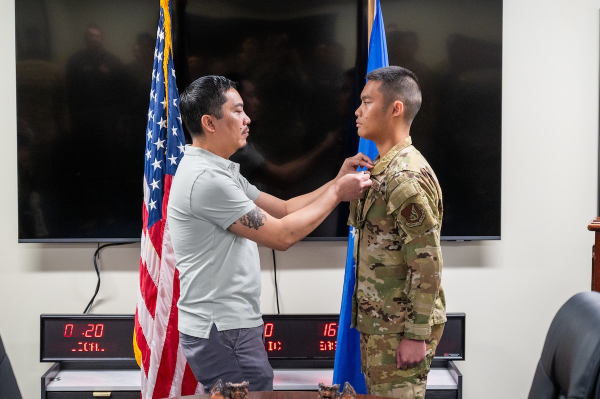 Retired U.S. Air Force Senior Master Sgt. Jose Libunao, left, pins a ribbon on his son, Senior Airman Angelo Libunao, during a ceremony at Kadena Air Base, Feb. 19, 2026. Libunao now serves in the same Aeromedical Evacuation squadron where his father and uncle were assigned, continuing a family tradition of service in the Indo-Pacific. (U.S. Air Force photo by Airman 1st Class Francisco Huerta)