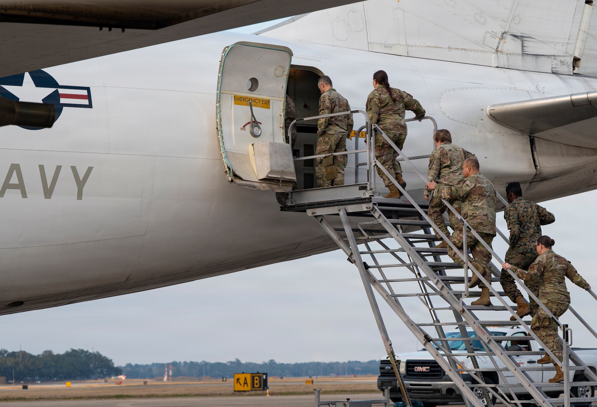 A group of service members in uniform enter a plane.
