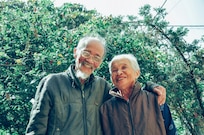 Elderly man and woman smile together in front of greenery