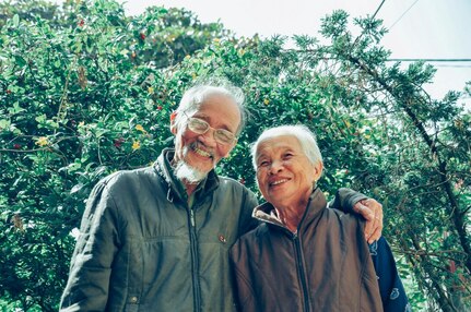 Elderly man and woman smile together in front of greenery