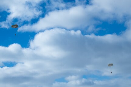 A man wearing a camouflage military uniform prepares for a parachute jump outside in a snow covered field.