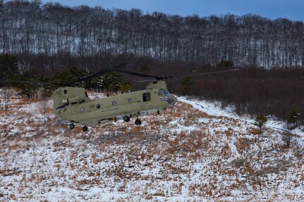 A man wearing a camouflage military uniform prepares for a parachute jump outside in a snow covered field.