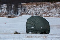 A man wearing a camouflage military uniform prepares for a parachute jump outside in a snow covered field.