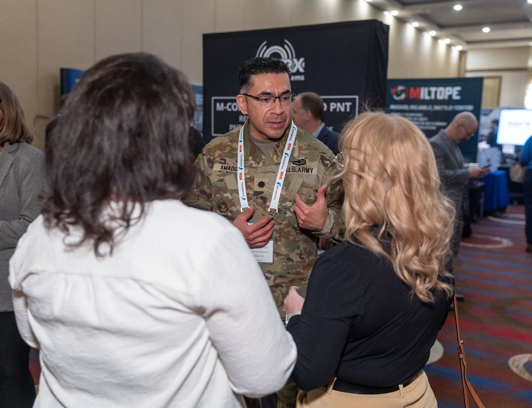 A man speaks to two women at a business event.