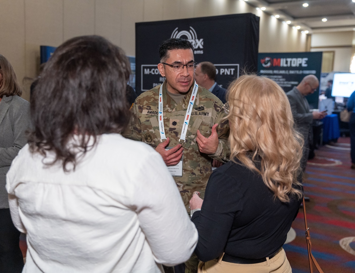 A man speaks to two women at a business event.