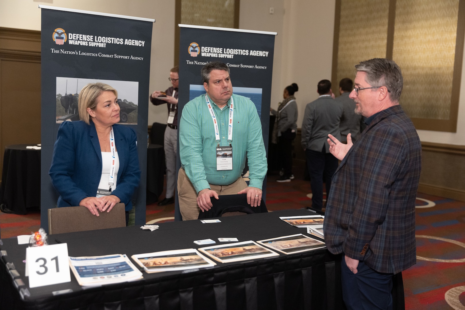 Two men and a woman have a discussion at a DLA booth in a conference setting.