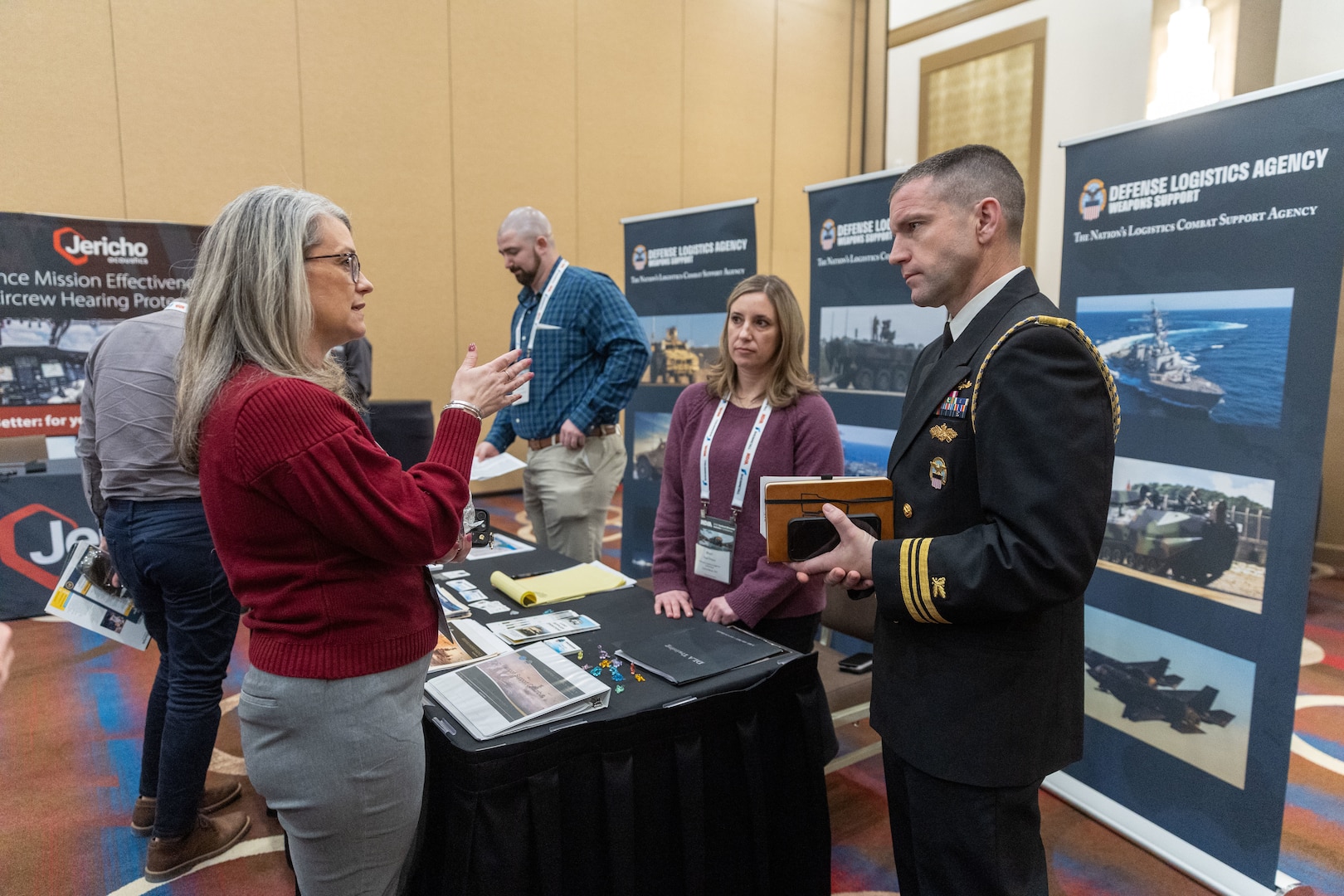 A group of people (men and women) have a discussion at a booth in a conference setting.