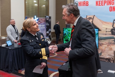 Defense Logistics Agency Weapons Support (Columbus) Commander Navy Rear Adm. Julie Treanor speaks with an industry partner. She is blond and he has graying hair and is in a suit.
