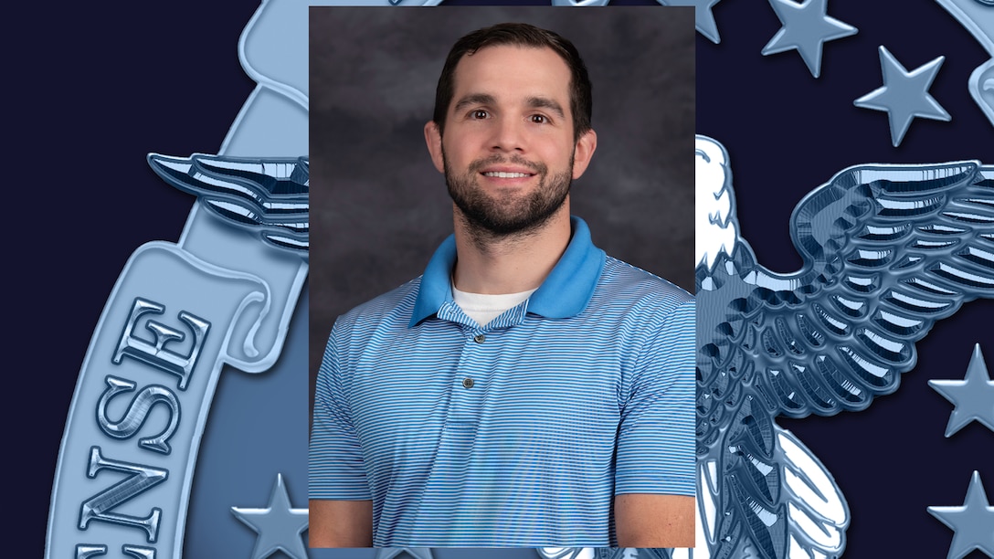 Headshot of man with dark hair and beard, wearing a light blue polo shirt