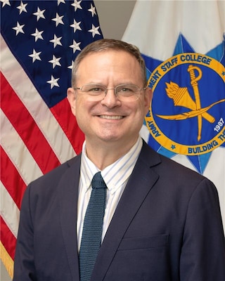 Civilian federal leader posed for a formal portrait with the Army Management Staff College emblem in the background.