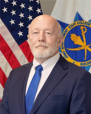 Civilian federal leader posed for a formal portrait with the Army Management Staff College emblem in the background.