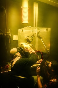 From left, Stephen Umeno, a nuclear welder, strikes an arc in the weld booth (behind the curtain) during a welding training qualification with Brad Morikawa, right, the nuclear welder supervisor, observing his technique in a Pearl Harbor Naval Shipyard and Intermediate Maintenance Facility weld shop Jan. 30, 2026.