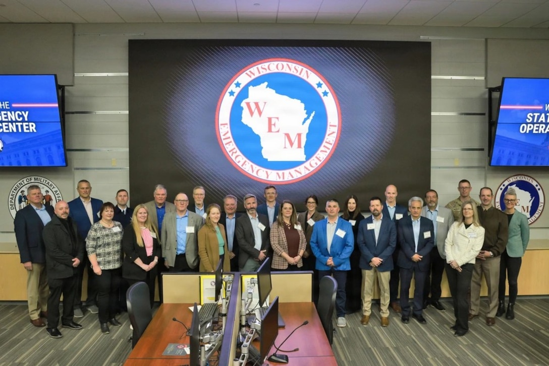 A group of people standing up front of a screen showing the Wisconsin Emergency Management logo