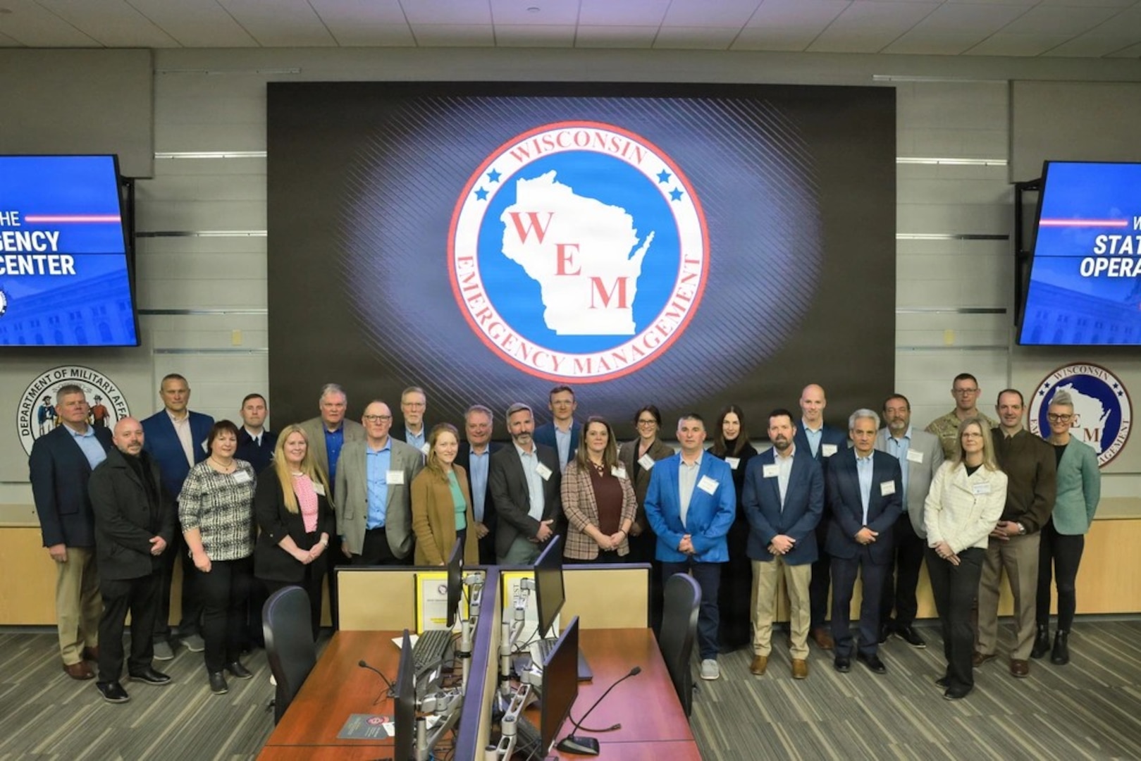 A group of people standing up front of a screen showing the Wisconsin Emergency Management logo