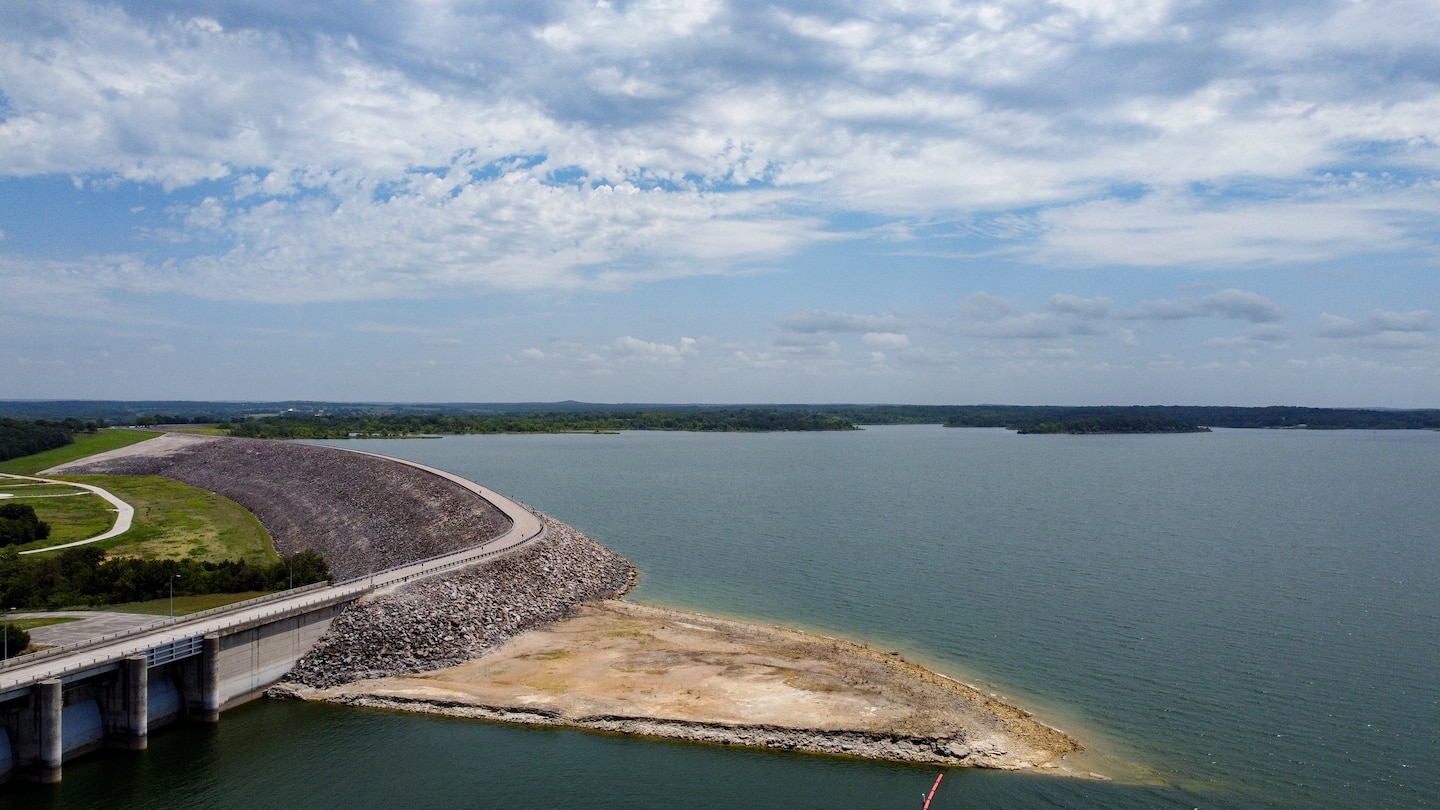 A body of water with sand in the foreground and a road on the left hand side.