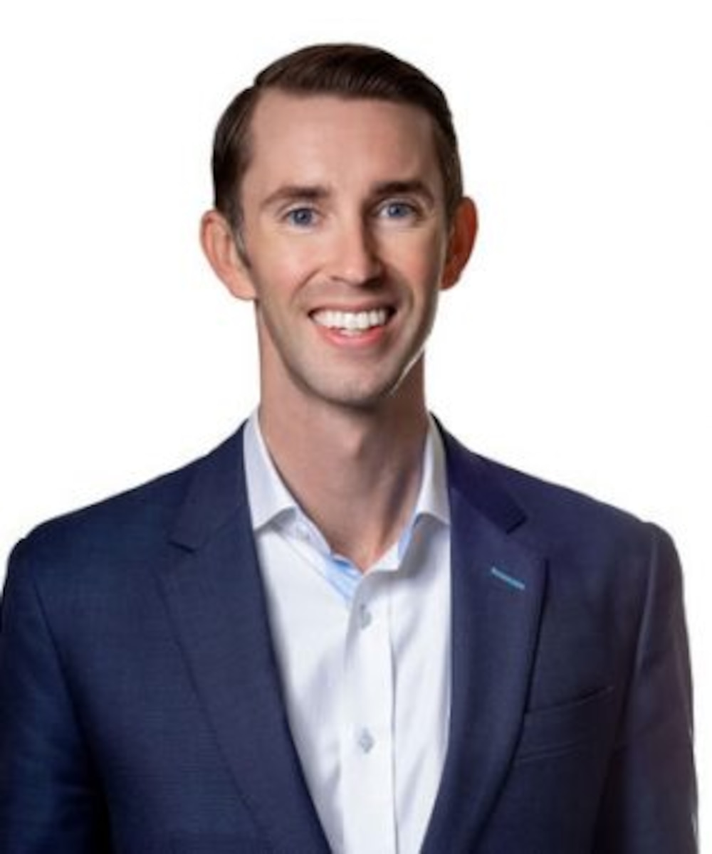 Posed photo of Air Force Maj Tyler Flansburg, project liaison, Air Force Accelerator in white button-up shirt with a blue blazer