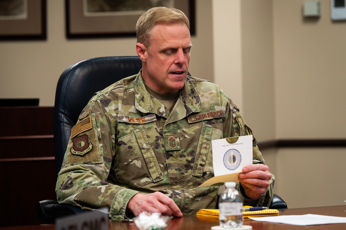 Man in Air Force camo sits at table and opens white envelope.