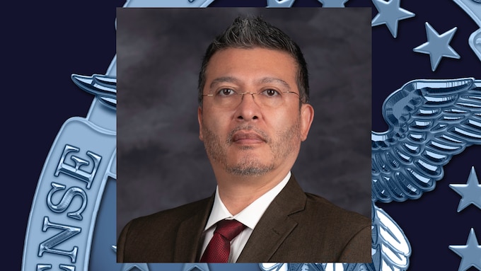 A photo of Walter Morales.He has a black suit on with a red tie. He has dark hair and glasses. 