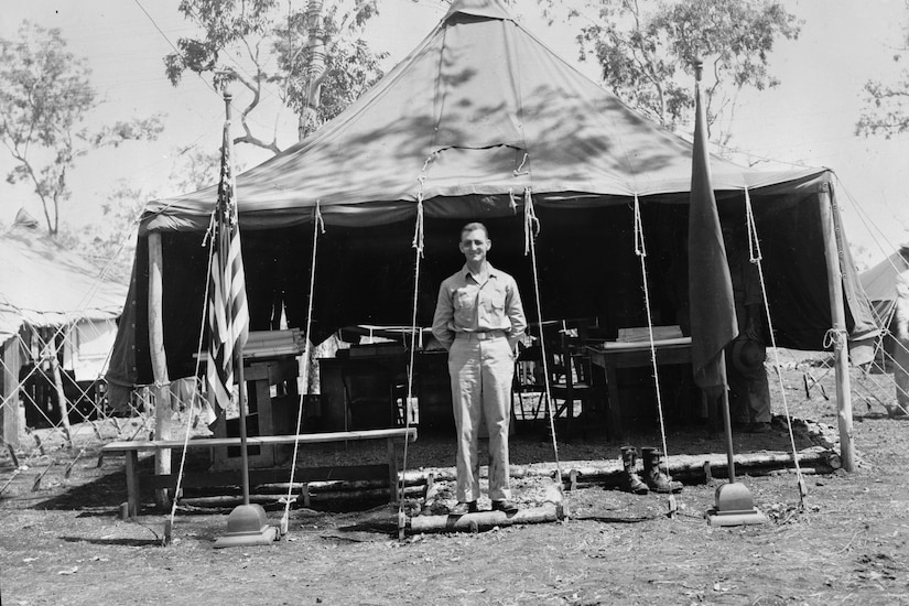A man stands in front of an open tent with an American flag posted out front.