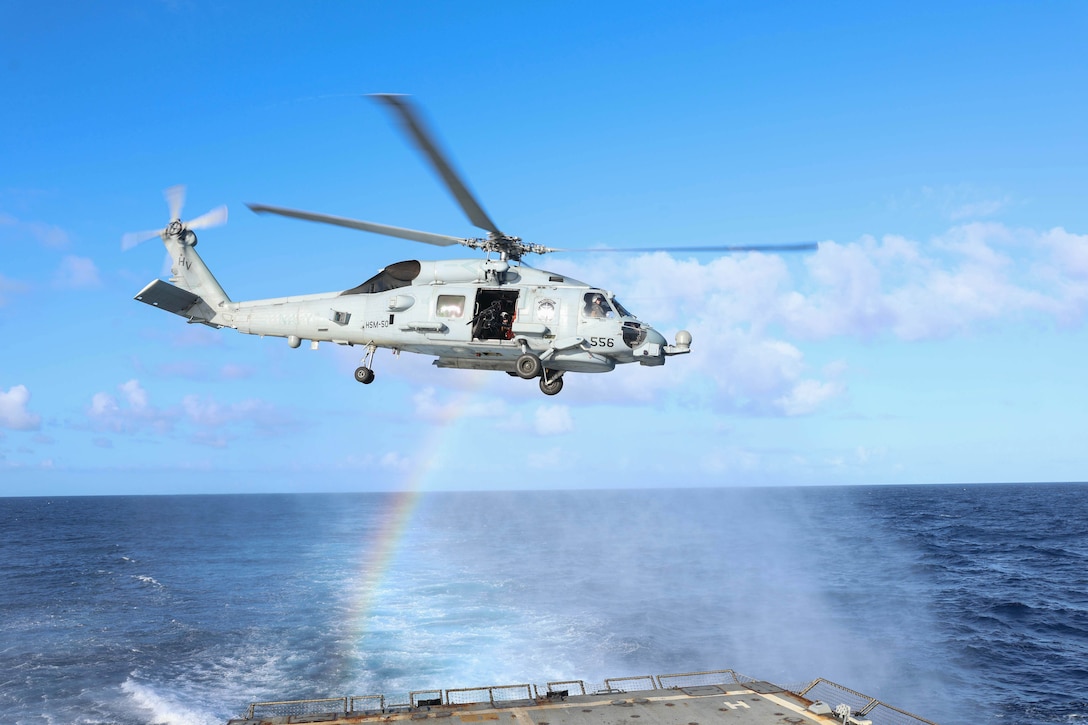 A helicopter flies above a ship at sea near a rainbow.