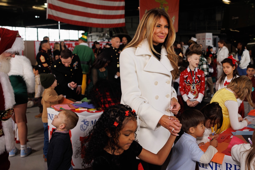 First Lady Melania Trump is led by a child to get her picture taken during her visit to Marine Corps Base Quantico, Virginia, Dec. 8, 2025. Mrs. Trump told a story to children in attendance, helped sort toys for Toys for Tots, and helped them make Christmas cards. (U.S. Marine Corps photo by Lance Cpl. David Brandes)