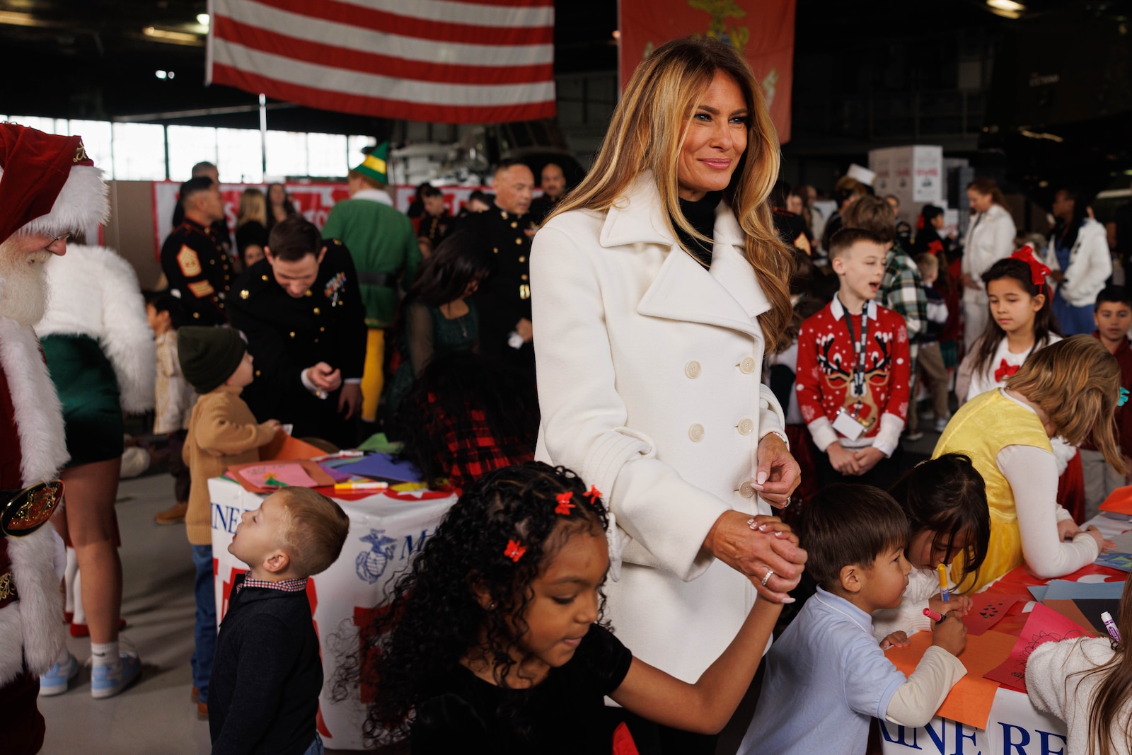 First Lady Melania Trump is led by a child to get her picture taken during her visit to Marine Corps Base Quantico, Virginia, Dec. 8, 2025. Mrs. Trump told a story to children in attendance, helped sort toys for Toys for Tots, and helped them make Christmas cards. (U.S. Marine Corps photo by Lance Cpl. David Brandes)