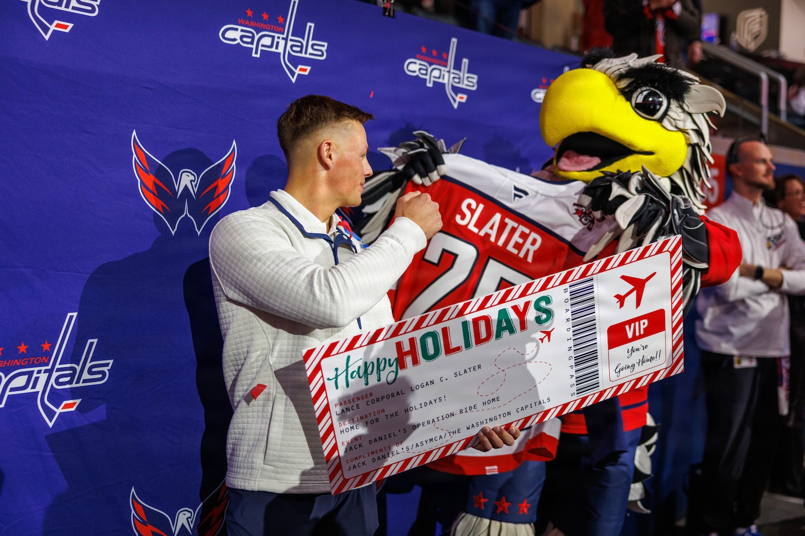 U.S. Marine Corps Lance Cpl. Logan Slater, a military police officer with Security Battalion, is gifted a plane ticket home and Washington Capital merchandise by Slapshot, the Washington Capitals mascot, during a hockey game between the Washington Capitals and Carolina Hurricanes at Capital One Arena in Washington, D.C. Dec. 11, 2025. Slater was gifted a plane ticket home and Washington Capital merchandise from the Armed Services Young Man’s Christian Association’s Operation Ride Home. Operation Ride Home provides travel assistance to service members and their families, helping them travel home for the holidays. The program, open to active duty and reserve personnel from ranks E-1 to E-5, aims to strengthen military families by bridging gaps that can prevent holiday travel. (U.S. Marine Corps photo by Lance Cpl. Federico Marquez)
