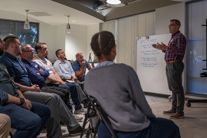 a speaker stands while talking to a group seated in chairs