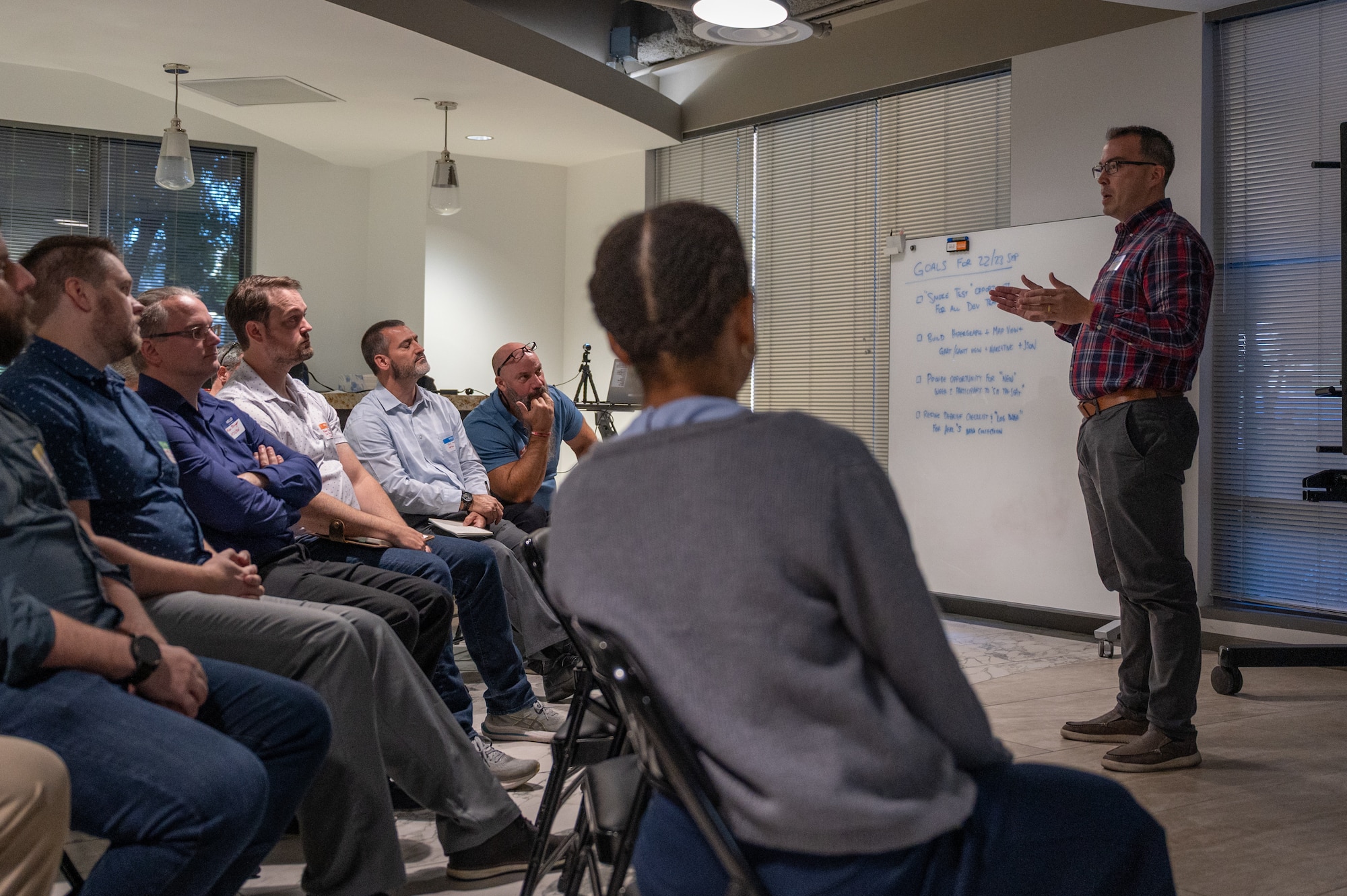 a speaker stands while talking to a group seated in chairs